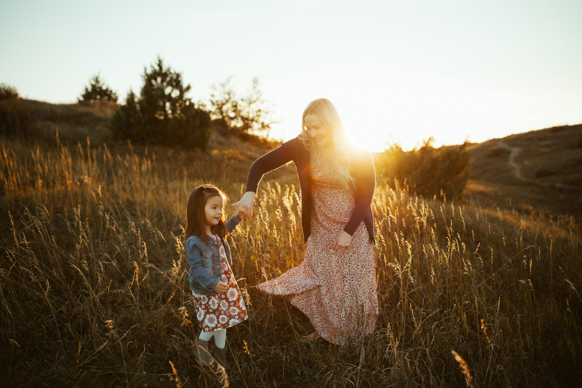 mom and daughter dancing on a grassy hill at sunset

