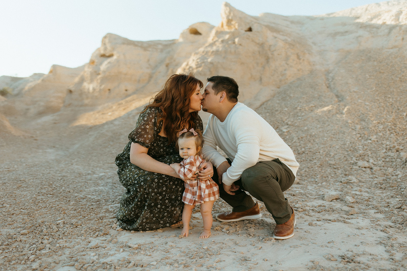 mom and dad kiss while holding baby girl