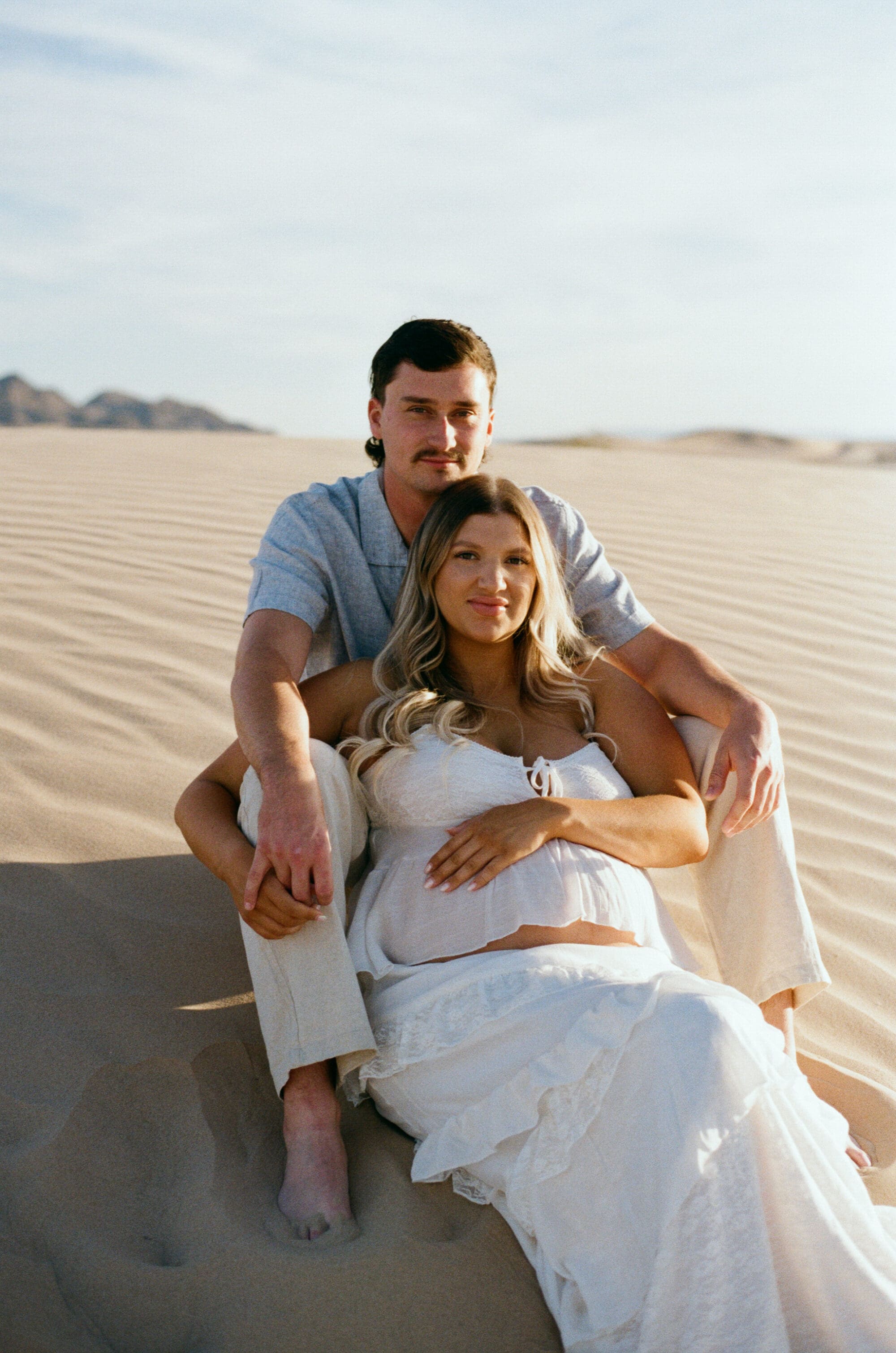 Film maternity photographer Las Vegas captures couple sitting at sand dunes